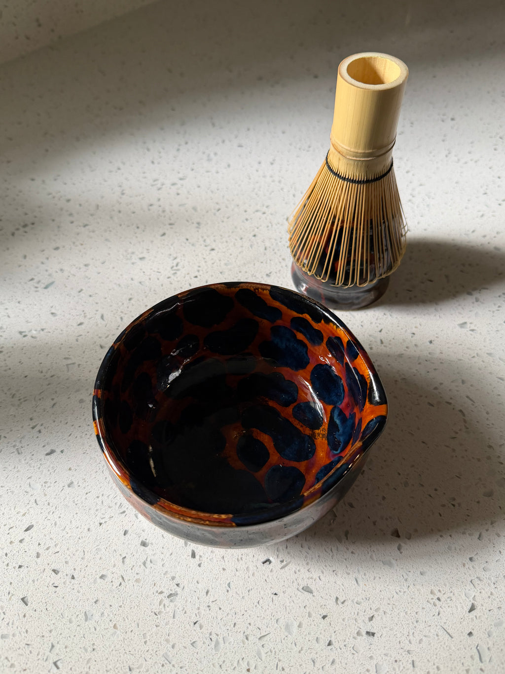 Ceramic bowl with a tortoiseshell pattern and bamboo whisk on a speckled surface